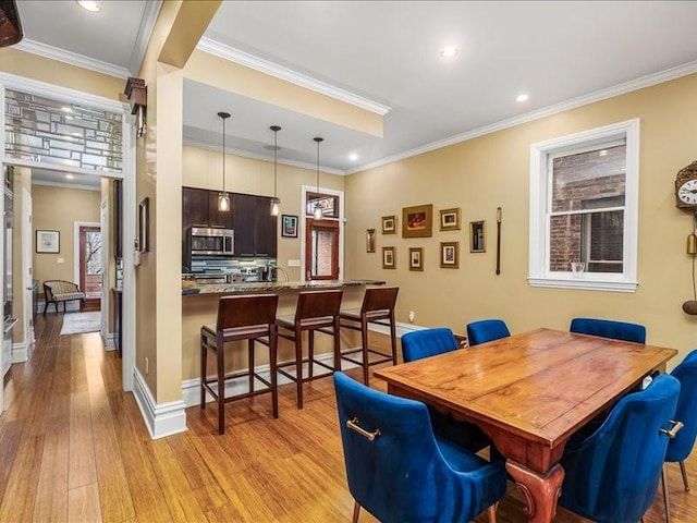 dining room featuring light wood-style flooring, ornamental molding, baseboards, and recessed lighting