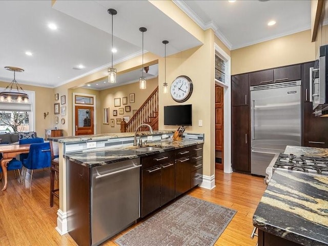 kitchen featuring decorative light fixtures, stainless steel appliances, light wood-style flooring, a sink, and dark stone counters