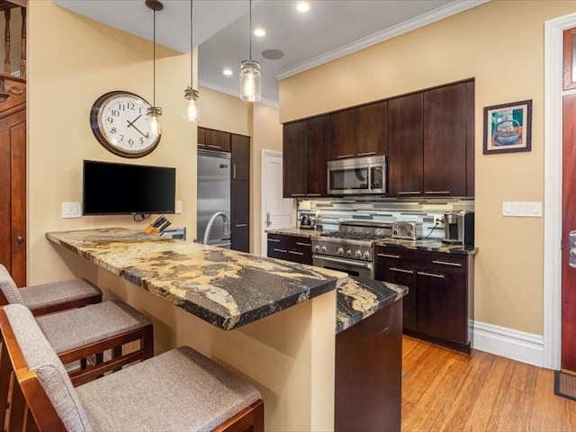 kitchen featuring dark brown cabinetry, a peninsula, high quality appliances, a kitchen bar, and crown molding