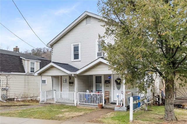 view of front facade with covered porch, a shingled roof, a front yard, and cooling unit