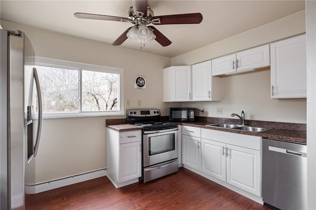 kitchen featuring stainless steel appliances, dark wood-style flooring, a sink, white cabinets, and dark countertops