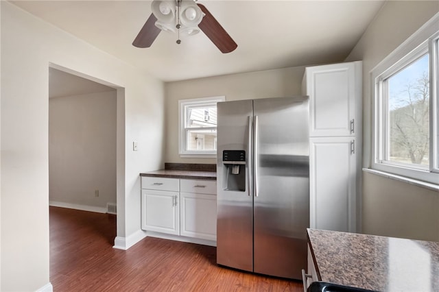 kitchen featuring wood finished floors, baseboards, white cabinets, dark countertops, and stainless steel fridge