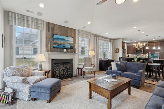 living room with visible vents, recessed lighting, a fireplace, light wood finished floors, and a chandelier