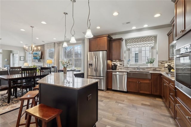 kitchen featuring light stone countertops, a sink, decorative backsplash, appliances with stainless steel finishes, and a center island