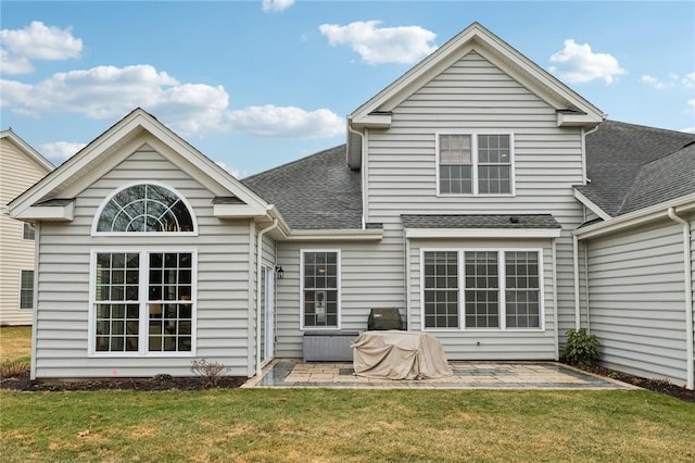 rear view of house with a patio, a lawn, and a shingled roof