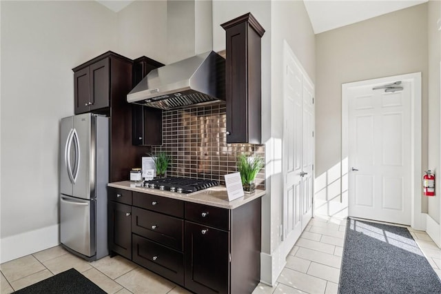 kitchen featuring light countertops, dark brown cabinetry, appliances with stainless steel finishes, wall chimney range hood, and tasteful backsplash