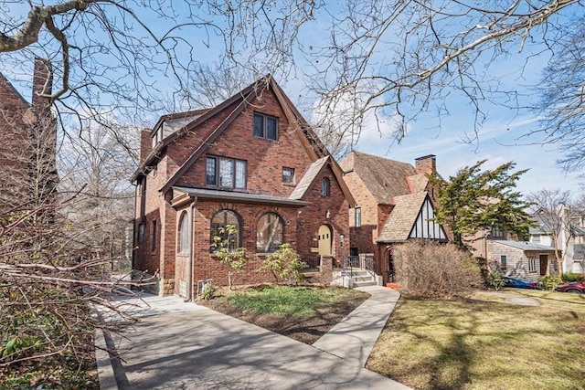 english style home with brick siding, a front lawn, and a chimney