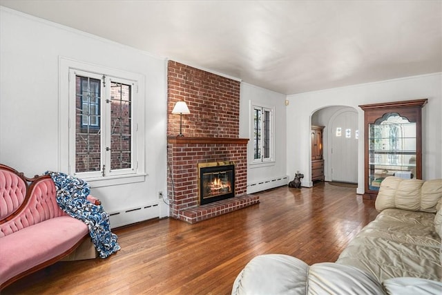 living room with a brick fireplace, wood-type flooring, arched walkways, and baseboard heating