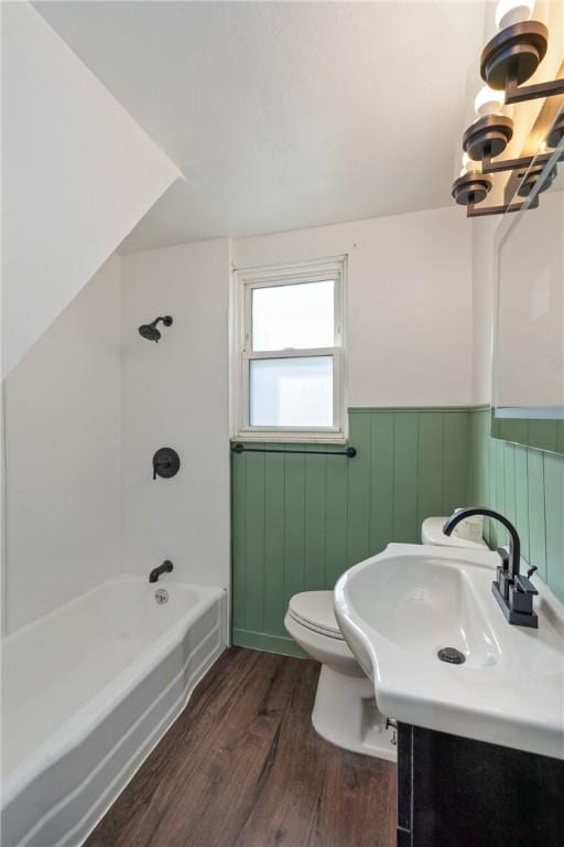 full bath featuring toilet, wood finished floors, vanity,  shower combination, and wainscoting