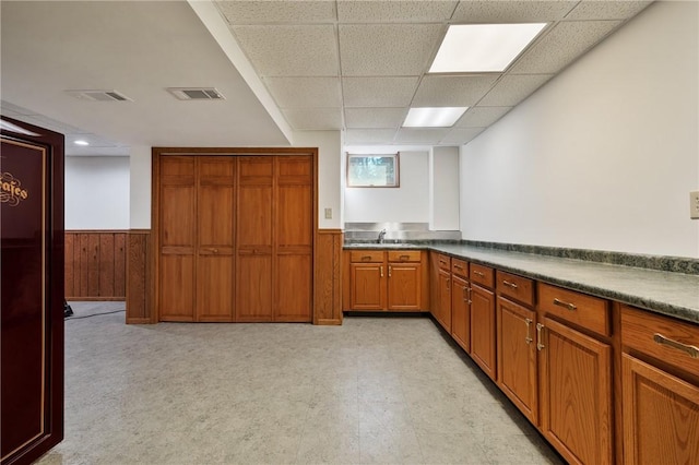 kitchen with wooden walls, visible vents, dark countertops, a wainscoted wall, and brown cabinets