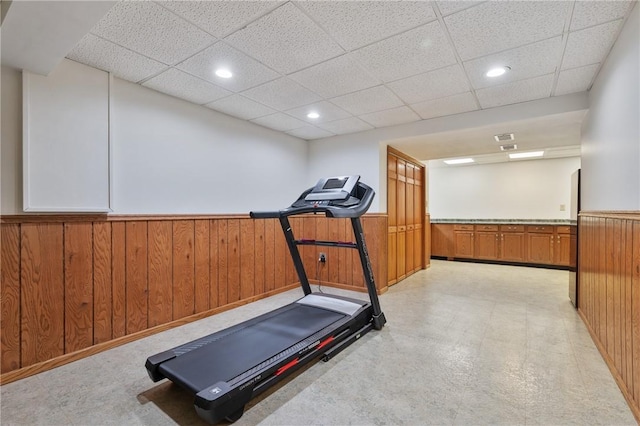 exercise room with a drop ceiling, wainscoting, light floors, wood walls, and recessed lighting