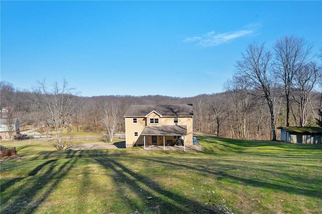 rear view of property with a patio area, a wooded view, and a lawn