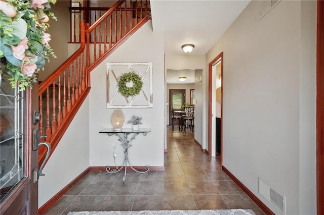 entrance foyer with dark tile patterned floors, baseboards, stairs, and visible vents