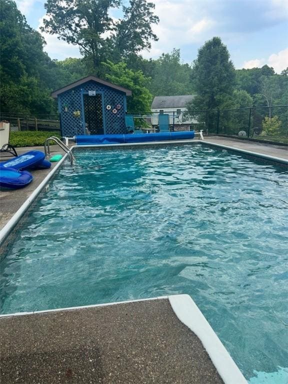 pool with a patio area, fence, and an outbuilding