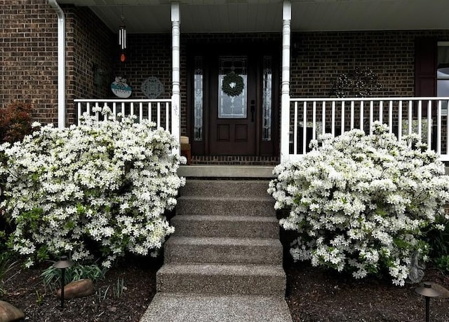 doorway to property featuring covered porch and brick siding