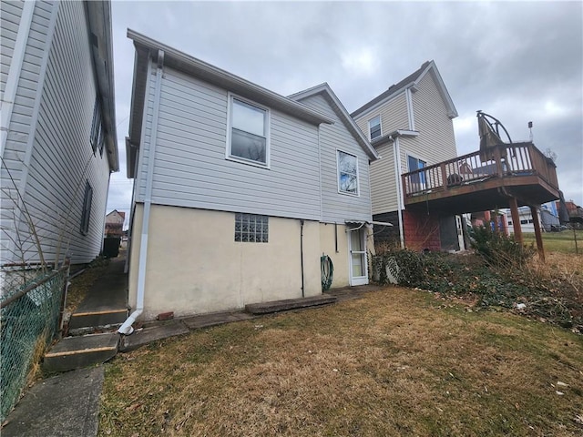 back of house with a wooden deck, a lawn, stucco siding, and fence