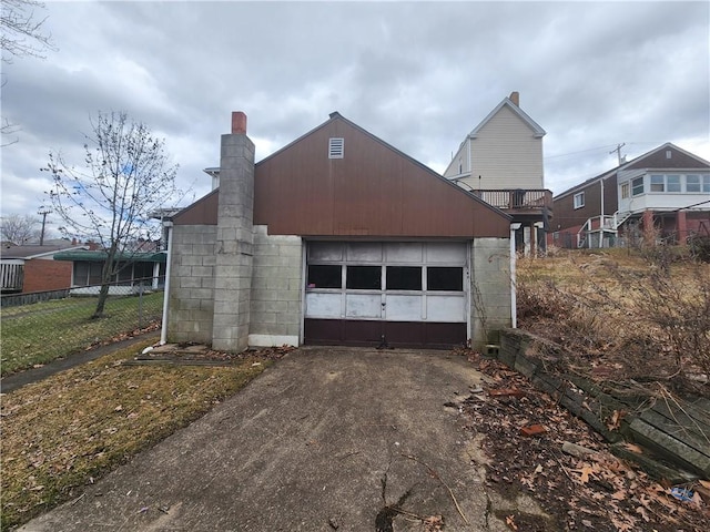 view of front facade with concrete block siding, fence, aphalt driveway, a chimney, and a detached garage