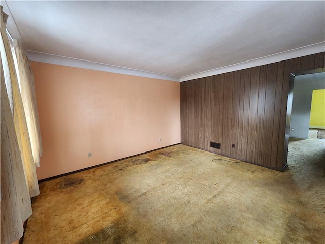 empty room with baseboards, visible vents, carpet floors, ornamental molding, and wood walls