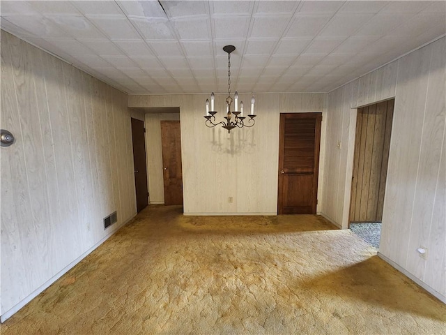 unfurnished dining area featuring visible vents, a notable chandelier, wood walls, and carpet flooring