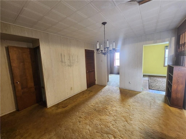 unfurnished dining area with wooden walls, a notable chandelier, and carpet