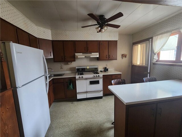 kitchen featuring under cabinet range hood, a sink, wallpapered walls, white appliances, and light countertops