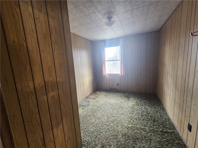 carpeted empty room with visible vents and wood walls