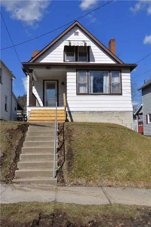 bungalow featuring stairway, a front yard, covered porch, and a chimney