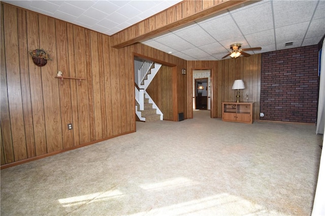 unfurnished living room featuring stairs, wooden walls, carpet flooring, and visible vents