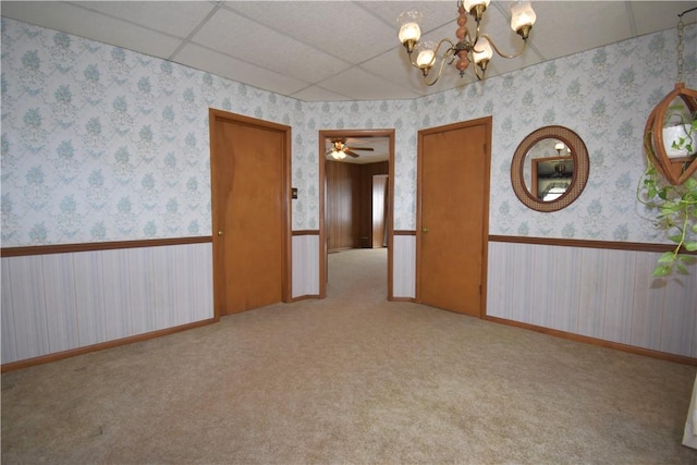 spare room with a wainscoted wall, carpet floors, wallpapered walls, an inviting chandelier, and a drop ceiling