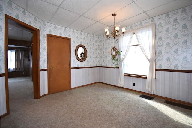 carpeted spare room featuring wallpapered walls, an inviting chandelier, a paneled ceiling, and wainscoting