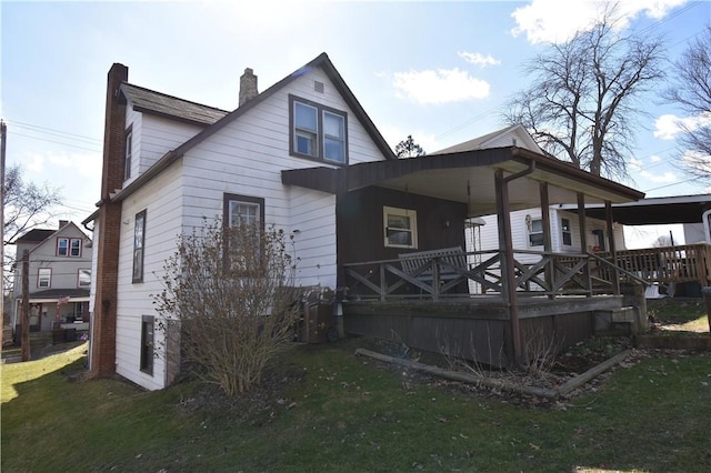 rear view of house featuring a chimney, covered porch, and a lawn