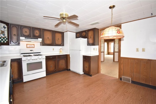 kitchen featuring under cabinet range hood, wainscoting, white appliances, and light wood-style floors