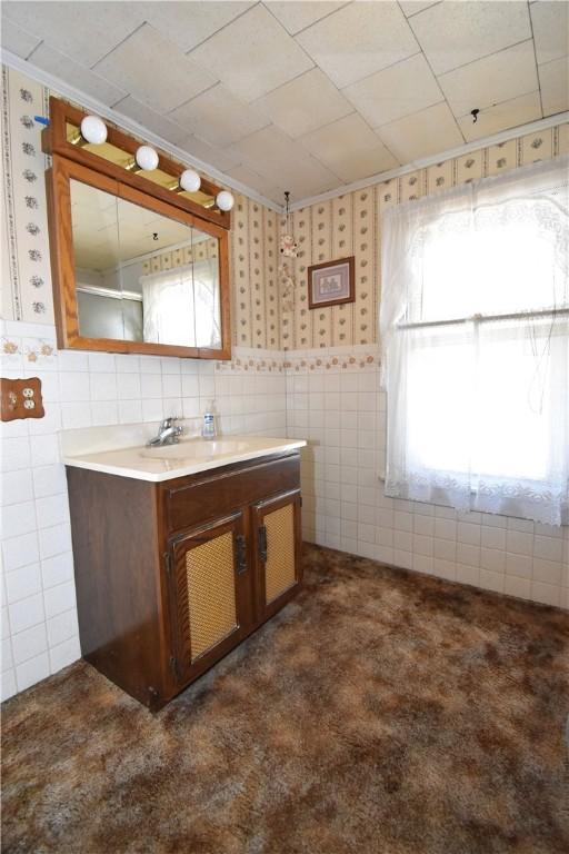 bathroom featuring tile walls, vanity, and wallpapered walls