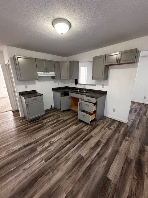 kitchen with dark countertops, gray cabinetry, under cabinet range hood, a textured ceiling, and dark wood-style flooring