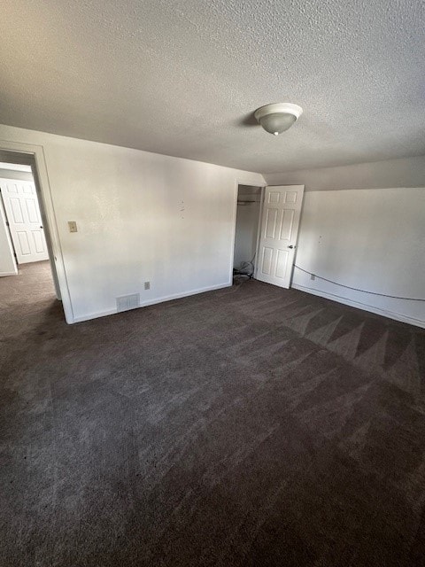 unfurnished room featuring visible vents, a textured ceiling, baseboards, and dark colored carpet