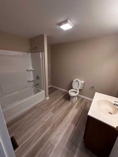 full bath featuring toilet, wood finished floors,  shower combination, baseboards, and vanity