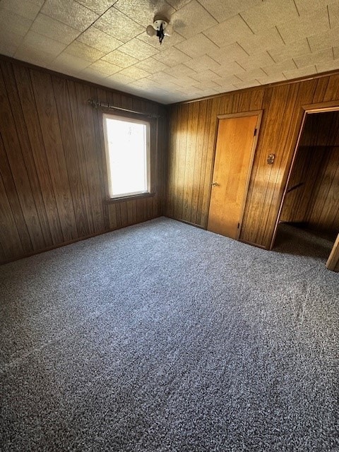 unfurnished bedroom featuring carpet flooring and wood walls