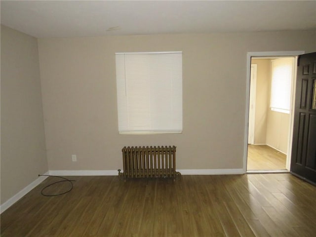 empty room with radiator, wood finished floors, and baseboards