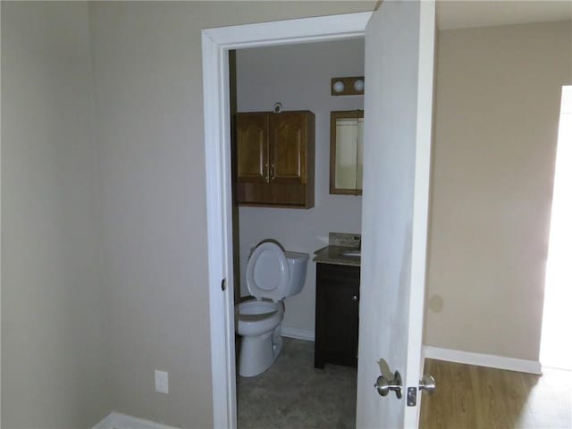 bathroom featuring vanity, toilet, wood finished floors, and baseboards