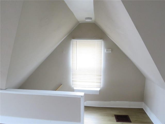 additional living space with vaulted ceiling, visible vents, baseboards, and wood finished floors