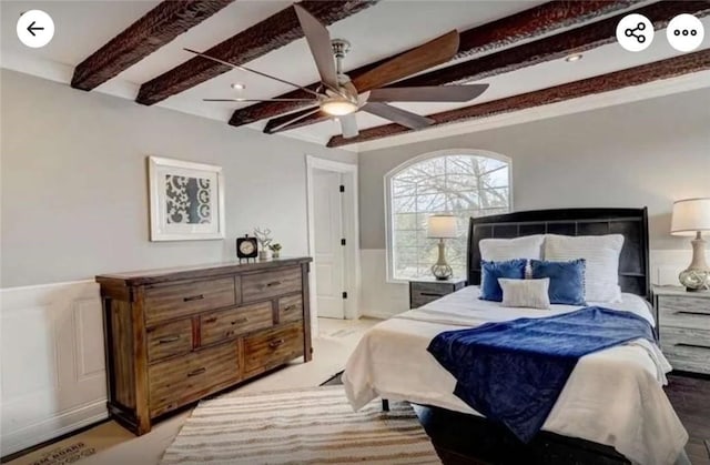 bedroom featuring beam ceiling, a decorative wall, wainscoting, and a ceiling fan