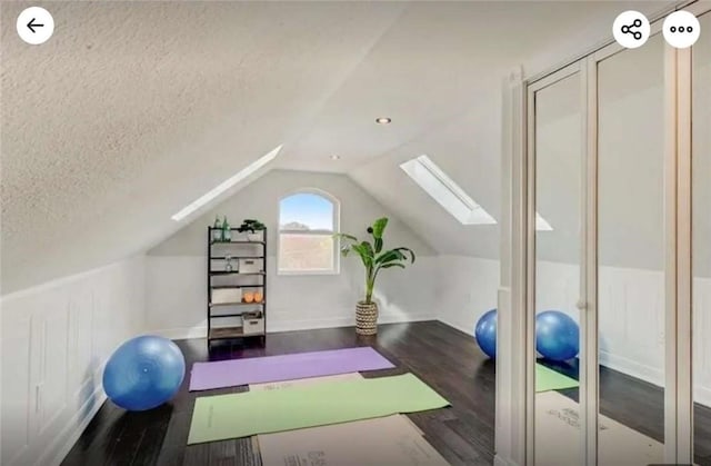 exercise room with lofted ceiling with skylight, a textured ceiling, and wood finished floors