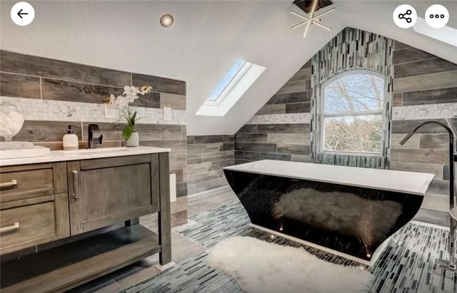 full bathroom featuring a soaking tub, vaulted ceiling with skylight, and vanity