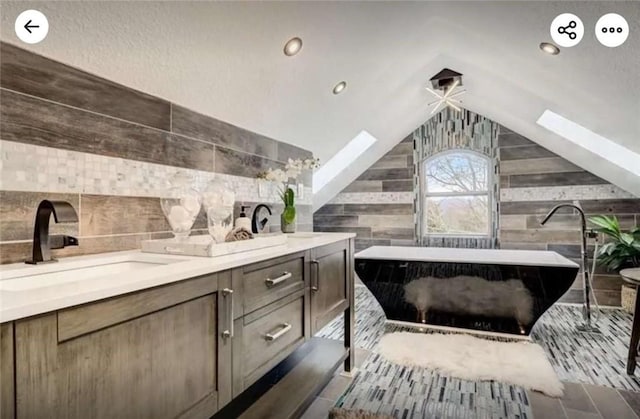 full bath featuring backsplash, lofted ceiling with skylight, double vanity, a soaking tub, and a sink