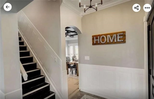 stairway with arched walkways, a chandelier, wainscoting, and crown molding