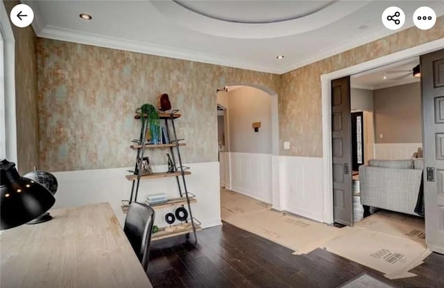 interior space featuring ornamental molding, a tray ceiling, wood finished floors, arched walkways, and wainscoting