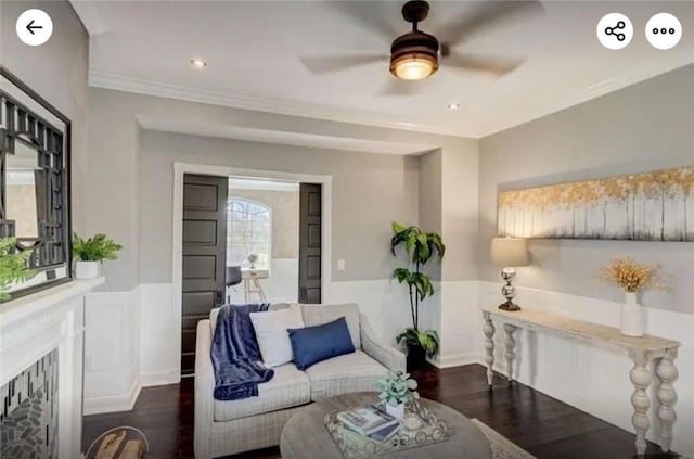 living room with ceiling fan, ornamental molding, wainscoting, a fireplace, and wood finished floors