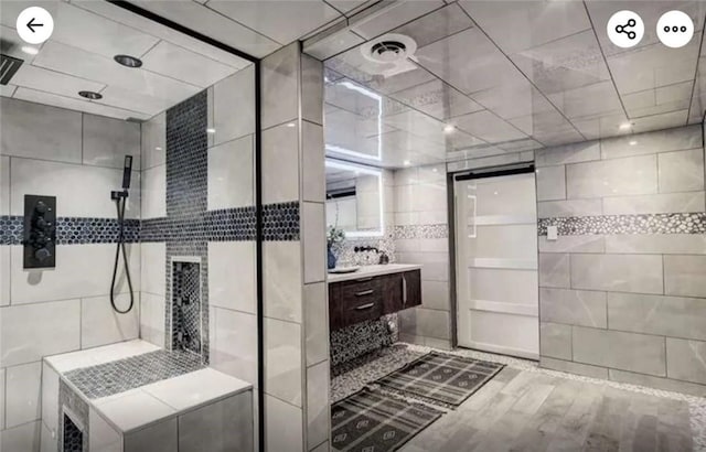 bathroom with vanity, wood finished floors, visible vents, a tile shower, and tile walls