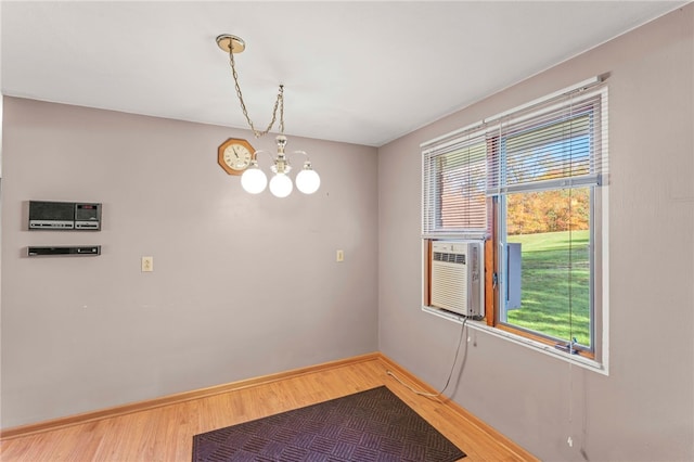 unfurnished room with an inviting chandelier, cooling unit, baseboards, and light wood-type flooring