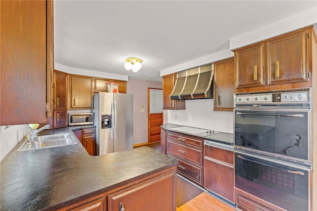 kitchen with a sink, dark countertops, stainless steel appliances, a peninsula, and wall chimney range hood